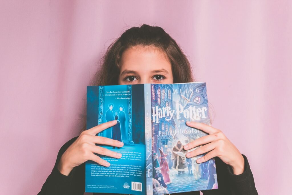pexels-photo-11340339-11340339 A young girl poses with a Harry Potter book against a pink backdrop, capturing a candid reading moment.